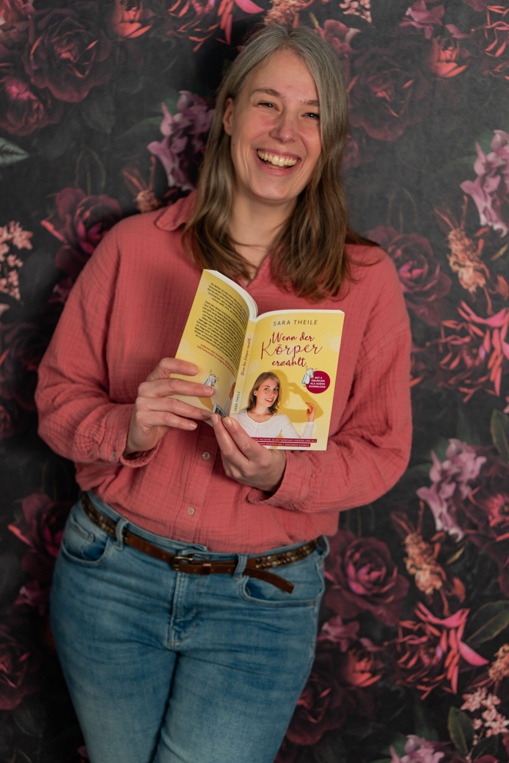 Sara hält ihr Buch aufgeschlagen in der Hand und lacht